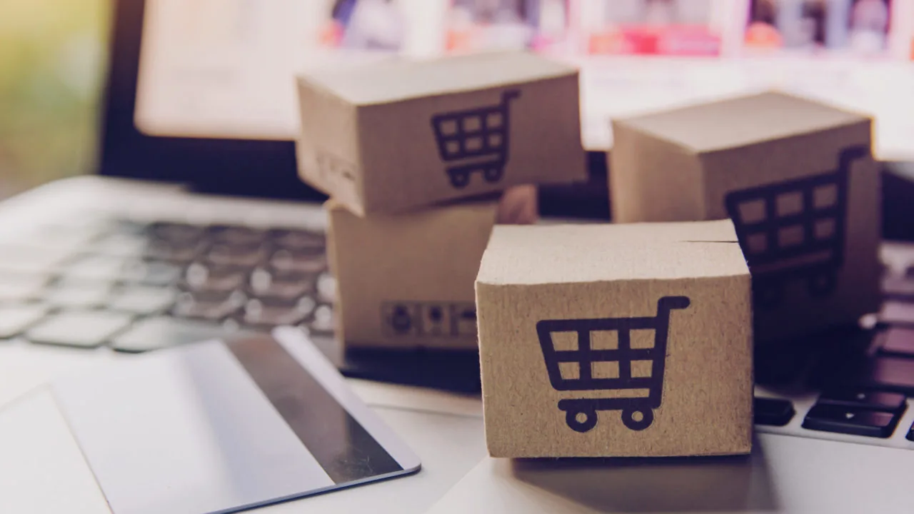 Cajas de cartón con símbolo de carrito sobre teclado de laptop junto a una tarjeta bancaria.