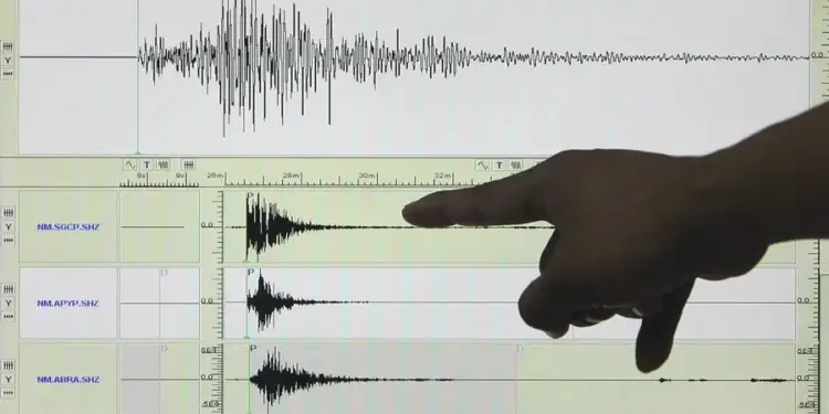 Una mano señala una pantalla de ordenador que muestra múltiples gráficos de ondas sísmicas, con escalas de tiempo y amplitud visibles. Los gráficos representan datos de monitoreo en tiempo real.