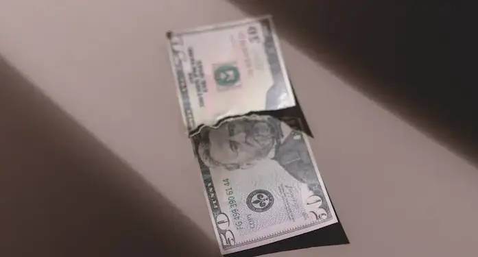 Un billete de cincuenta dólares estadounidenses, con el retrato de Ulysses S. Grant, aparece rasgado por la mitad sobre una superficie clara. Se lee "COPY".