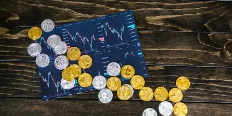 Monedas doradas y plateadas de criptomonedas sobre gráficos de trading digitales en una mesa de madera.