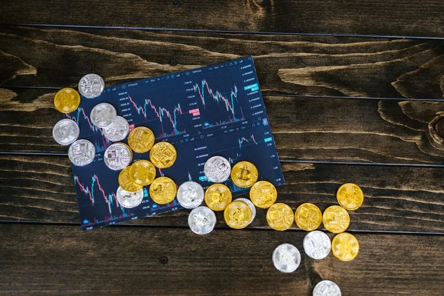 Monedas doradas y plateadas de criptomonedas sobre gráficos de trading digitales en una mesa de madera.