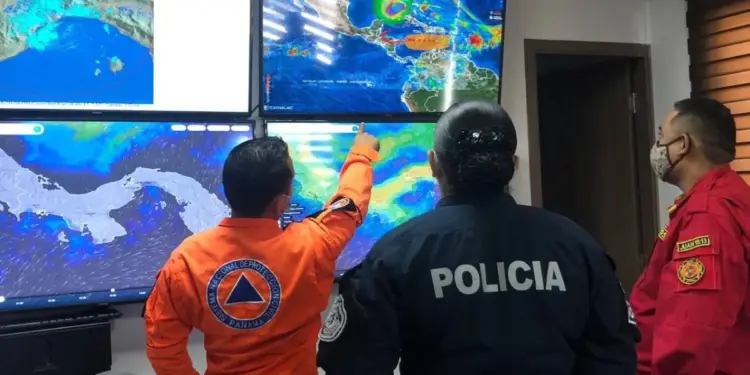 Personal de emergencia, policía y bomberos observando pantallas con mapas meteorológicos en un centro de control.