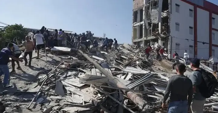 Grupo de personas trabajando y observando escombros y ruinas de un edificio derrumbado.