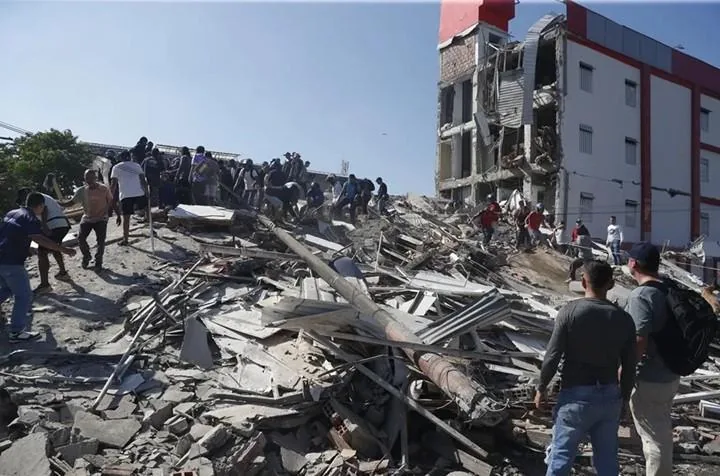 Grupo de personas trabajando y observando escombros y ruinas de un edificio derrumbado.