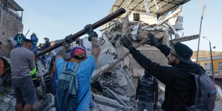 Hombres retiran escombros de un edificio colapsado. Voluntarios y personal de rescate trabajan entre ruinas, moviendo vigas y concreto.