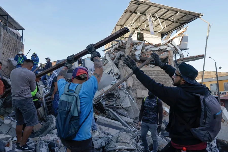 Hombres retiran escombros de un edificio colapsado. Voluntarios y personal de rescate trabajan entre ruinas, moviendo vigas y concreto.