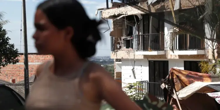 Una mujer en primer plano desenfocado y al fondo un edificio con daños estructurales en su fachada.