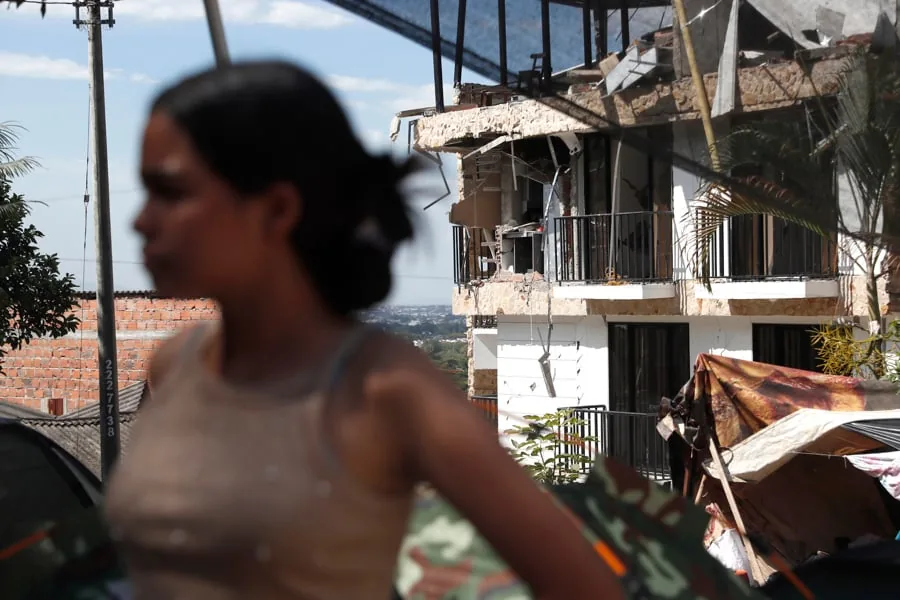 Una mujer en primer plano desenfocado y al fondo un edificio con daños estructurales en su fachada.
