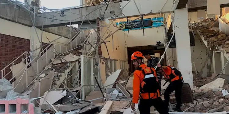 Rescatistas con equipo de seguridad inspeccionando un edificio con daños estructurales severos y escombros.