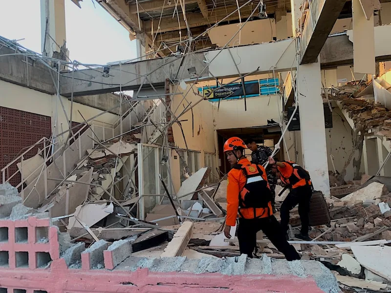 Rescatistas con equipo de seguridad inspeccionando un edificio con daños estructurales severos y escombros.