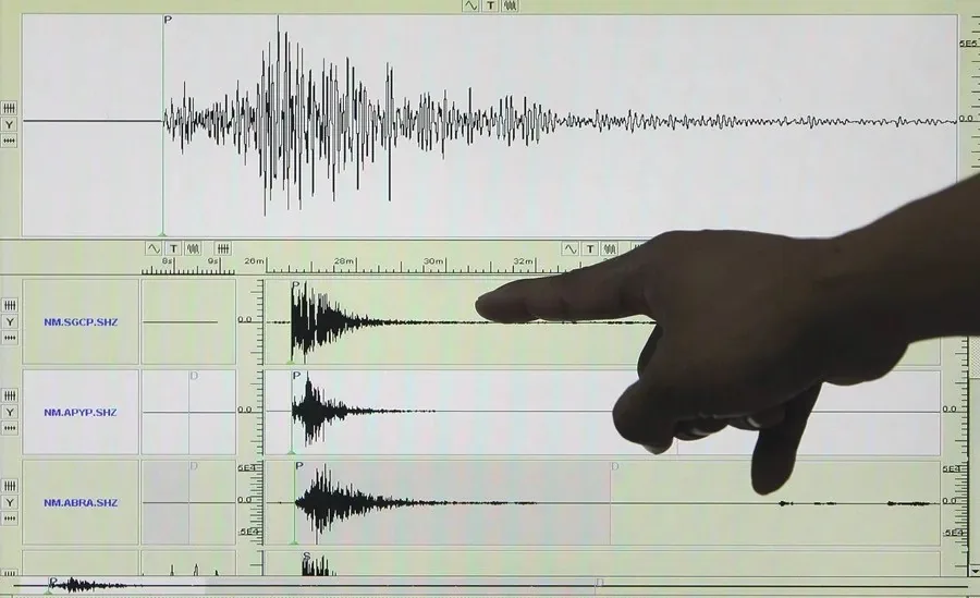 Mano señalando gráficos de ondas sísmicas y sismogramas en una pantalla de ordenador.