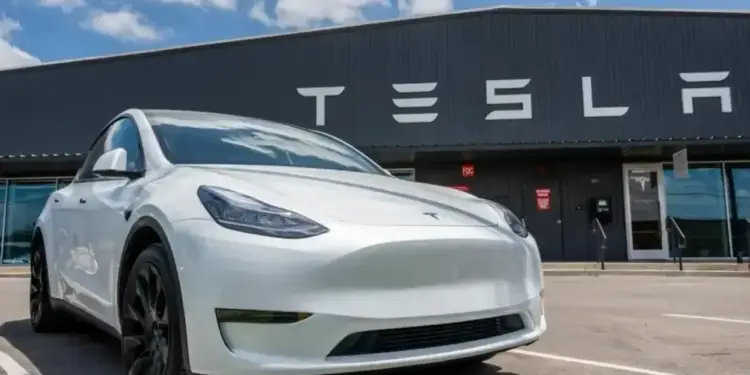 Automóvil eléctrico de color blanco estacionado en el exterior de un edificio con el letrero de Tesla.