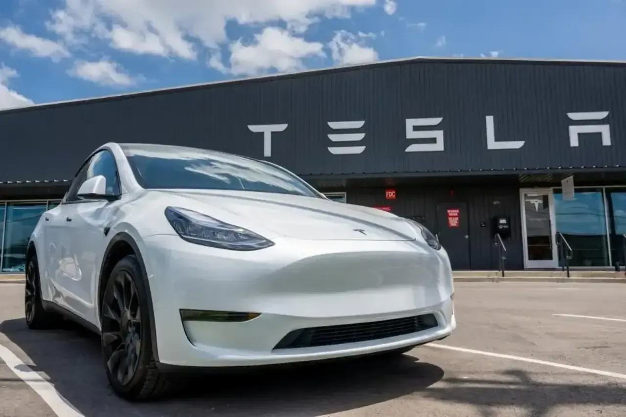 Automóvil eléctrico de color blanco estacionado en el exterior de un edificio con el letrero de Tesla.