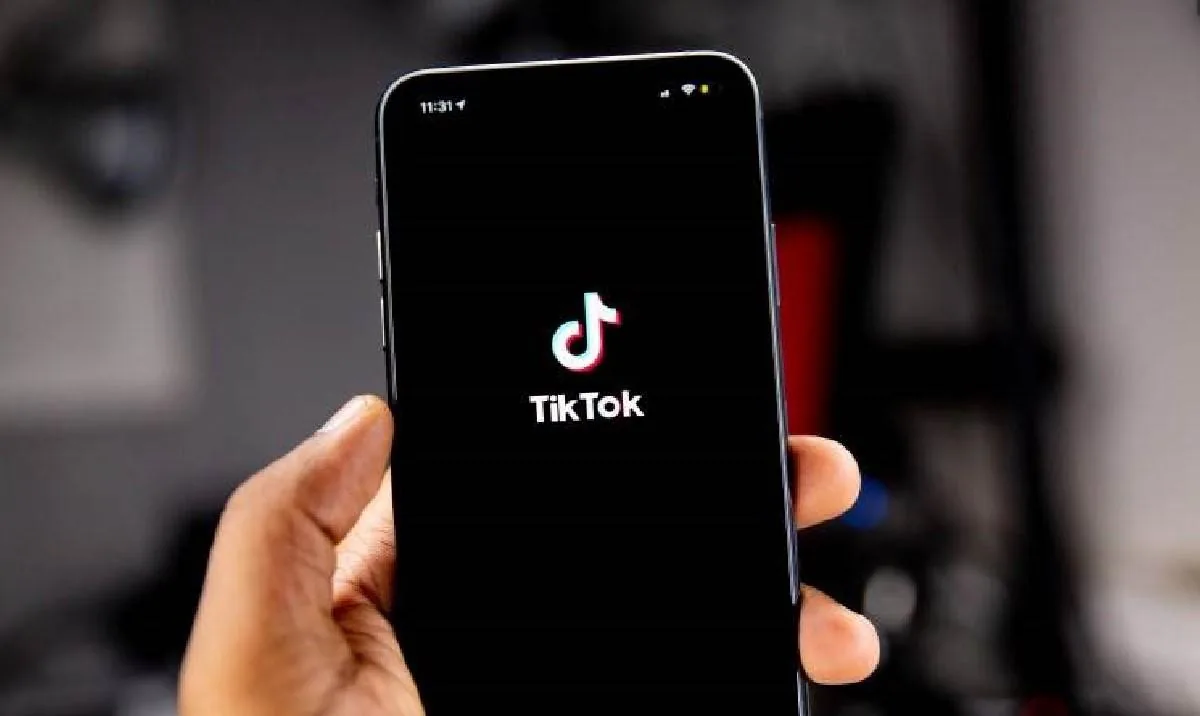 Mano sosteniendo un smartphone con el logo de TikTok en pantalla negra. La hora 11:31 es visible. Ilustra la presencia de la app en el ámbito digital y empresarial.