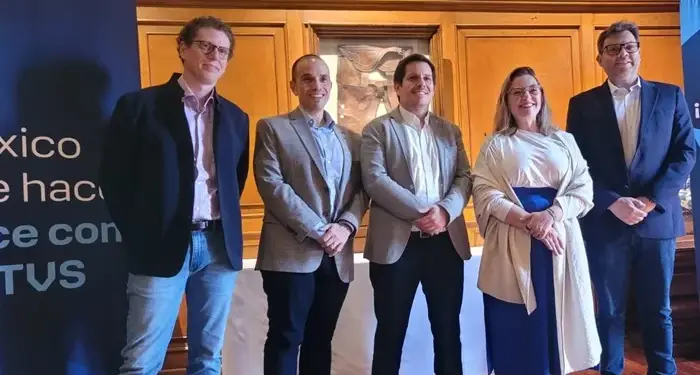 Grupo de cinco profesionales de pie en un evento empresarial frente a paneles informativos y paneles de madera.