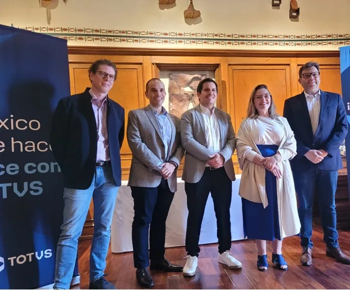 Grupo de cinco profesionales de pie en un evento empresarial frente a paneles informativos y paneles de madera.