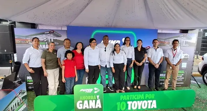 Grupo de personas sonrientes posando en un evento corporativo frente a un panel publicitario con la leyenda Ahorrá y Ganá