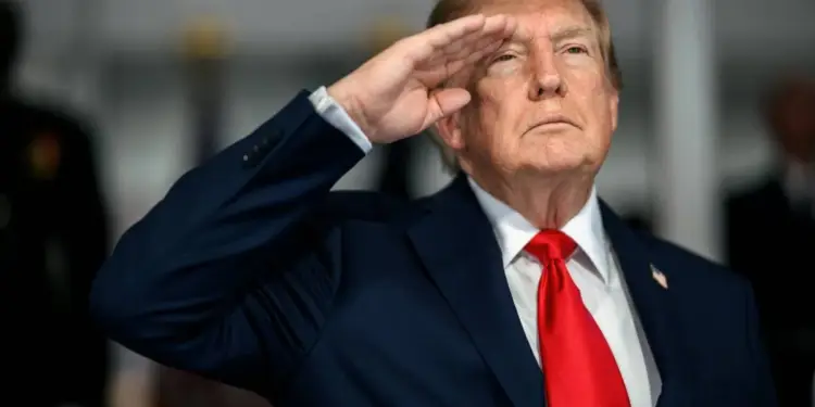 Donald Trump vestido con traje azul y corbata roja haciendo un saludo militar.