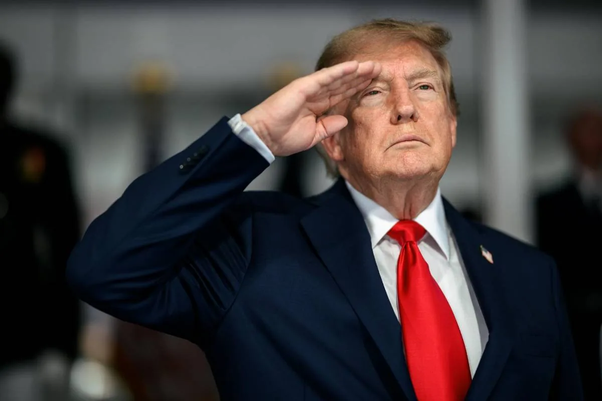 Donald Trump vestido con traje azul y corbata roja haciendo un saludo militar.