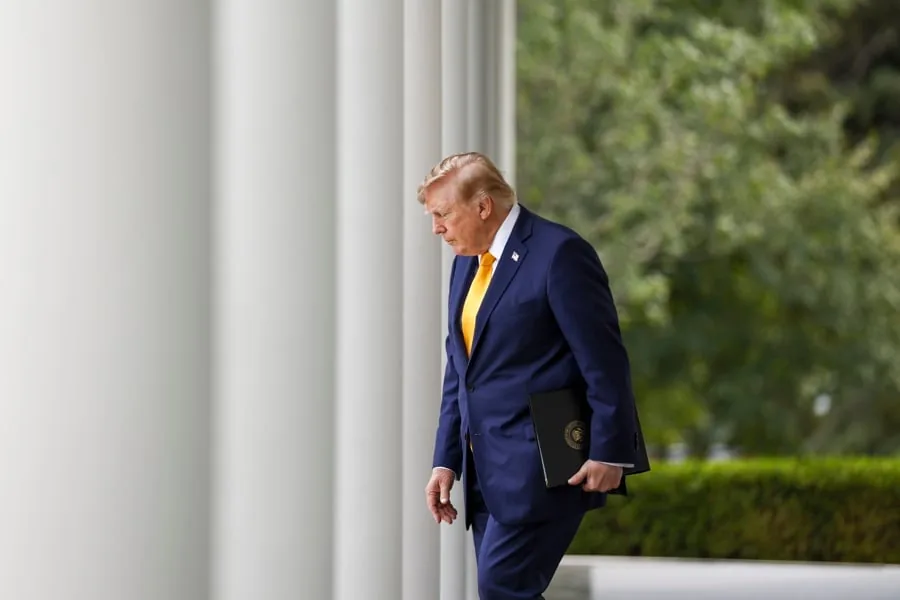 Hombre de negocios con traje azul oscuro y corbata amarilla caminando entre grandes columnas blancas.