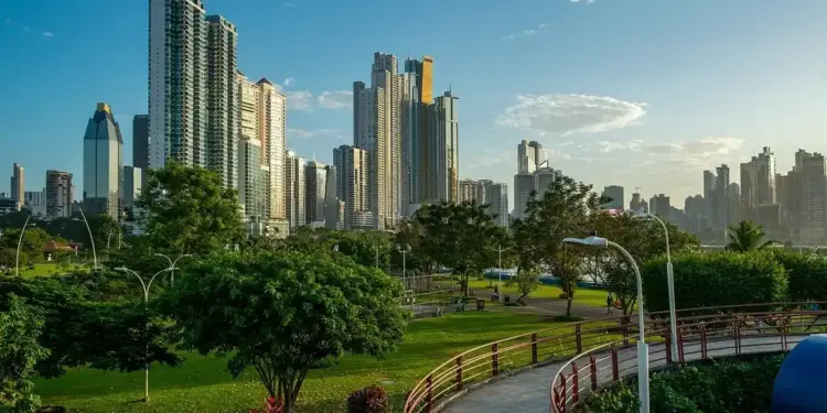 Paisaje urbano con rascacielos altos al fondo y un parque verde con senderos y árboles en primer plano bajo un cielo azul