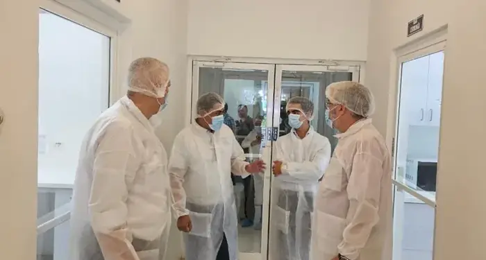 Cuatro profesionales con trajes de protección y mascarillas conversando en el pasillo de una instalación industrial.