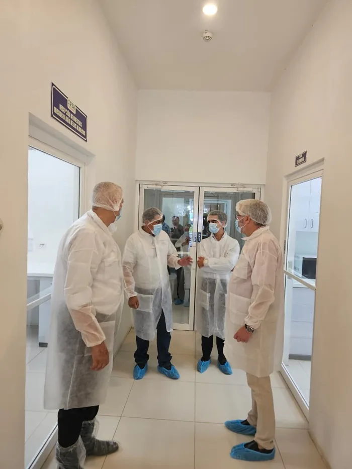Cuatro profesionales con trajes de protección y mascarillas conversando en el pasillo de una instalación industrial.
