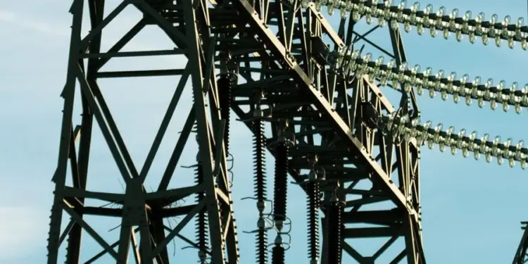 Estructura metálica de una torre de alta tensión con aisladores y cables eléctricos contra un cielo claro.