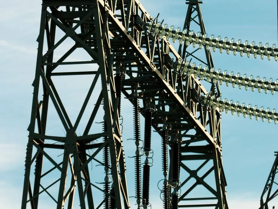 Estructura metálica de una torre de alta tensión con aisladores y cables eléctricos contra un cielo claro.