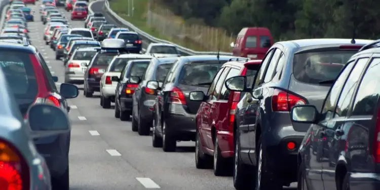 Vista trasera de una carretera con múltiples carriles llena de coches detenidos o moviéndose lentamente, formando un atasco. Se aprecian vehículos de diversos colores en una fila interminable bajo un cielo diurno.