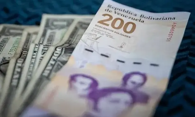 Primer plano de un billete de 200 bolívares venezolanos junto a varios billetes de dólar estadounidense, sobre una superficie azul texturizada.