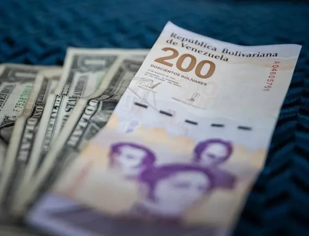 Primer plano de un billete de 200 bolívares venezolanos junto a varios billetes de dólar estadounidense, sobre una superficie azul texturizada.