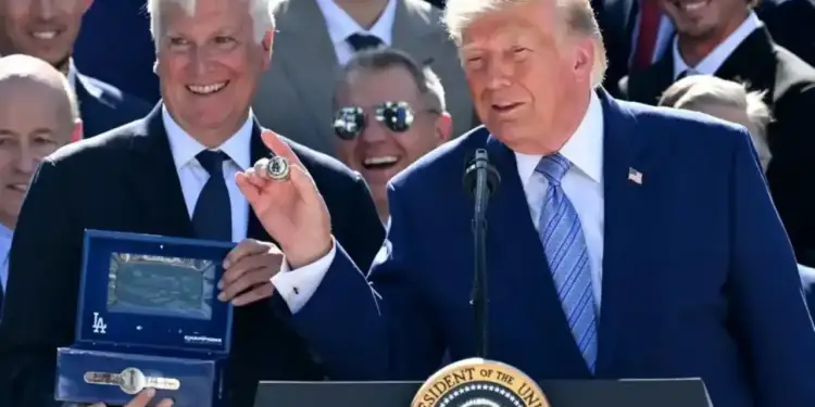 Donald Trump en podio presidencial y un hombre con cabello blanco mostrando un anillo de campeonato con logo 'LA' y una caja azul.
