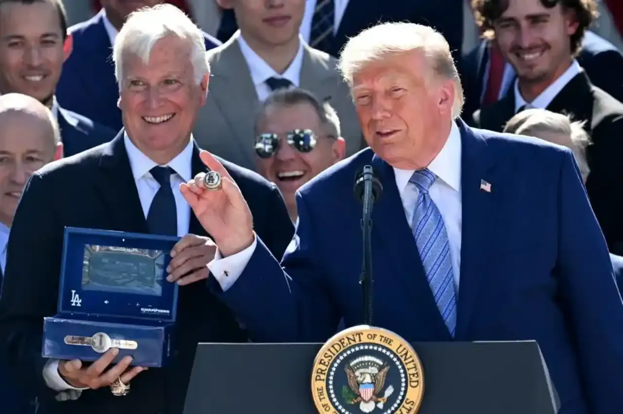 Donald Trump en podio presidencial y un hombre con cabello blanco mostrando un anillo de campeonato con logo 'LA' y una caja azul.