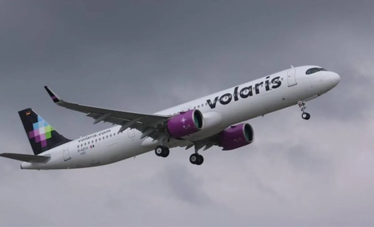 Avión de pasajeros blanco con motores morados y el logo 'Volaris' en el fuselaje, despegando bajo un cielo nublado.