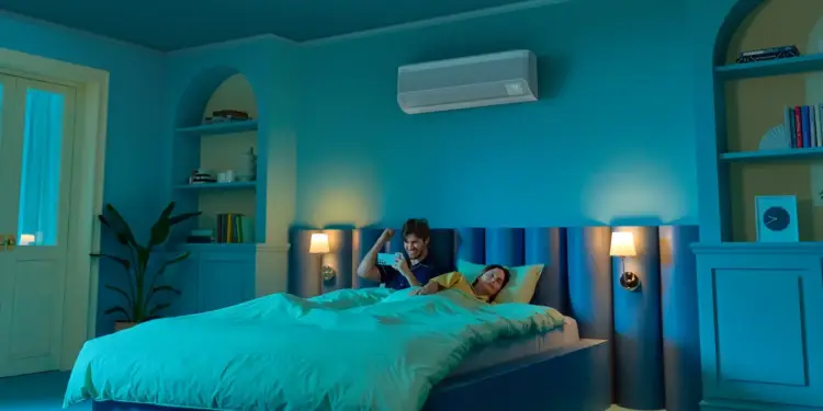 Pareja en una habitación iluminada de azul usando un teléfono móvil para controlar un aire acondicionado.