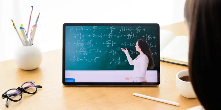 Persona de espaldas viendo una clase de matemáticas en una tablet sobre un escritorio de madera