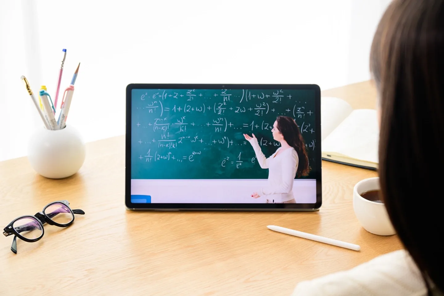 Persona de espaldas viendo una clase de matemáticas en una tablet sobre un escritorio de madera