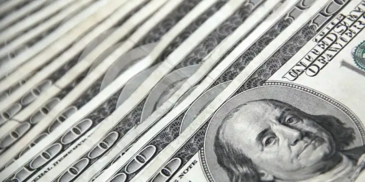 Primer plano en diagonal de varios billetes de cien dólares superpuestos, mostrando el retrato y números.