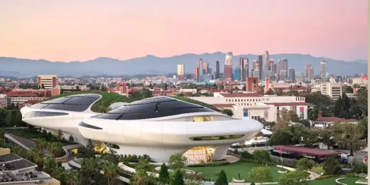 Vista panorámica de un edificio futurista blanco con techos verdes y paneles solares frente a un distrito financiero urbano al atardecer.