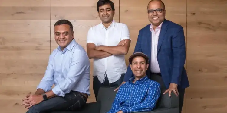 Cuatro hombres sonrientes posando en una oficina con fondo de paneles de madera.
