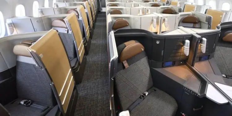 Vista interior de la cabina de clase ejecutiva en un avión con asientos reclinables individuales y pasillo central.