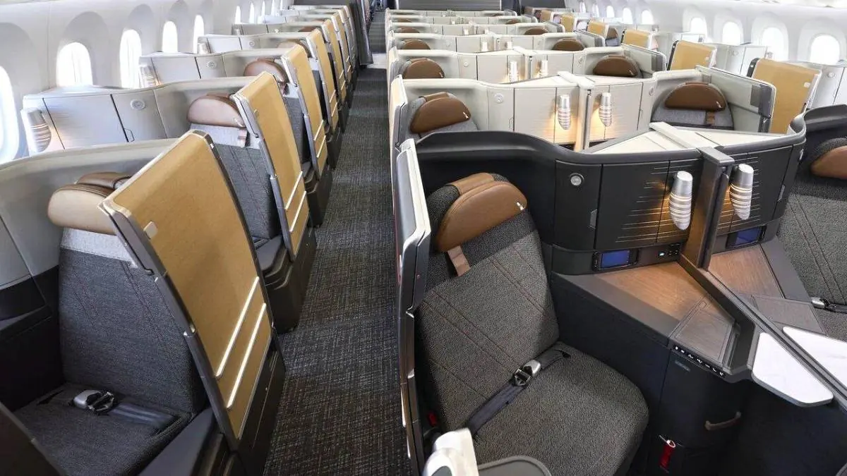Vista interior de la cabina de clase ejecutiva en un avión con asientos reclinables individuales y pasillo central.