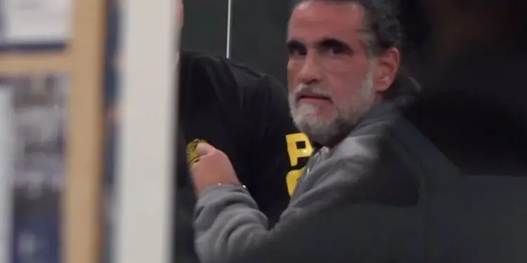 Primer plano de un hombre maduro con cabello oscuro y barba canosa mirando fijamente hacia la cámara.