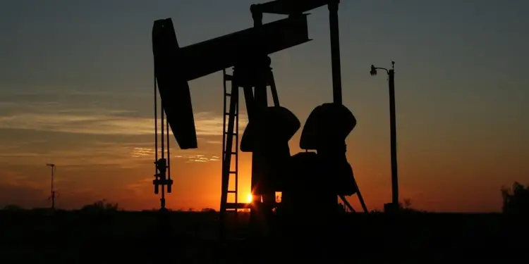 Silueta de una bomba de extracción petrolera mecánica contra un cielo de atardecer con tonos anaranjados y oscuros.