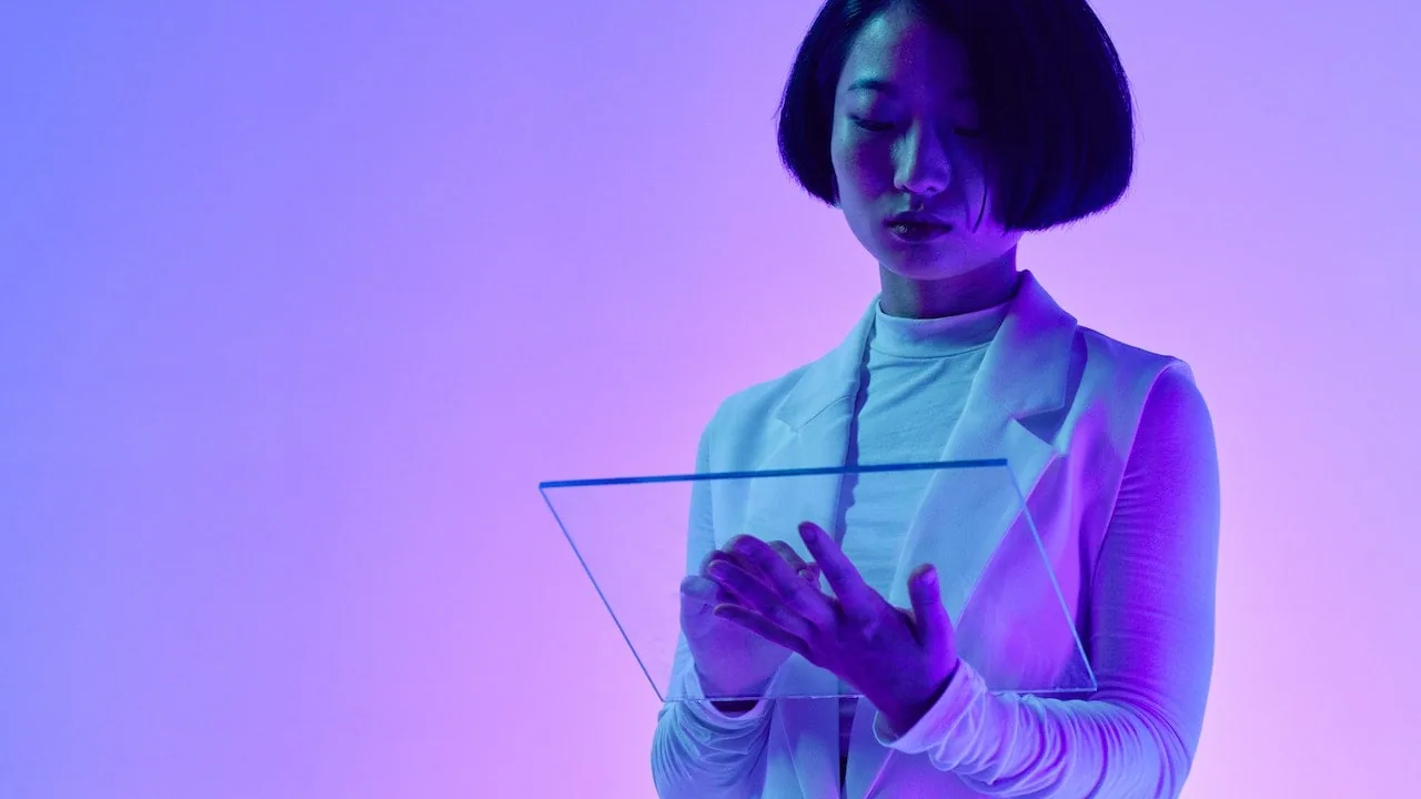 Mujer con cabello oscuro interactuando con una pantalla transparente futurista. Viste ropa profesional y está inmersa en un entorno de luz neón púrpura y azul, simbolizando innovación tecnológica en finanzas.