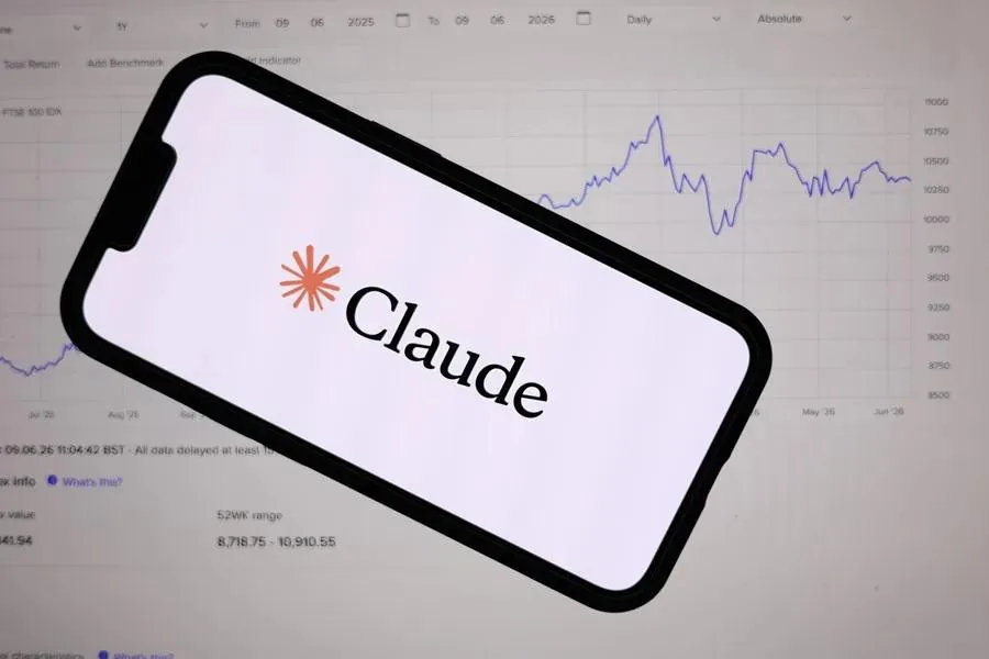 Un smartphone con el logo y nombre 'Claude' en pantalla, superpuesto sobre un monitor que muestra un gráfico de líneas financieras y datos de mercado.