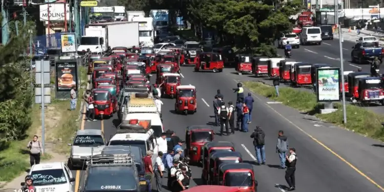 Congestionamiento vehicular con numerosos mototaxis rojos y personas reunidas en una carretera.