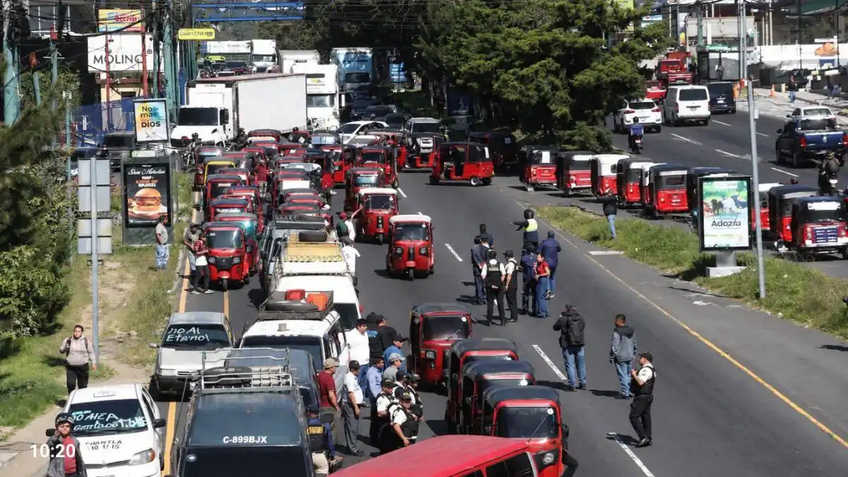 Congestionamiento vehicular con numerosos mototaxis rojos y personas reunidas en una carretera.