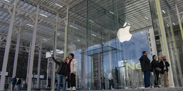 Personas tomando fotografías frente a una moderna tienda con fachada de cristal y una estructura metálica exterior.